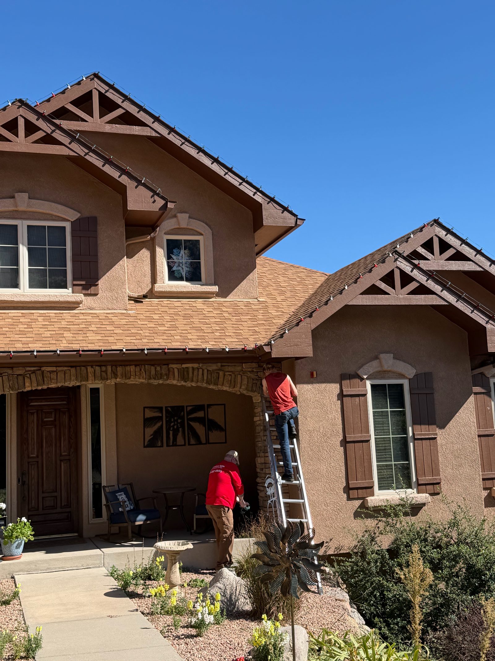 Our Front Range crew on ladder installing roofline Christmas lights by the front porch Our Front Range crew on ladder installing roofline Christmas lights by the front porch
